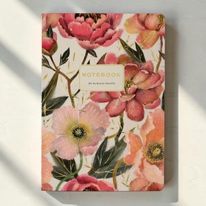 May include: A rectangular notebook featuring a white cover with a vibrant floral pattern of pink, peach, and red peonies and green leaves. The center includes a rectangular label with the text NOTEBOOK and BV by Bruno Visconti in gold.