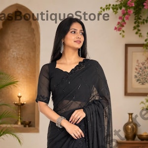 May include: A black saree featuring sheer fabric with intricate tonal embroidery and sequin embellishments. The garment includes a matching blouse with short sleeves and a scalloped neckline, draped elegantly to showcase the detailed border work.