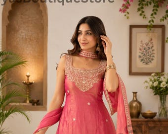 Könnte beinhalten: Ein ärmelloses pinkfarbenes Sharara-Set mit quadratischem Ausschnitt, aufwendiger Goldstickerei, passendem Dupatta und weit geschnittener Hose. Der Stoff hat einen dezenten Glanz und der Saum ist mit detaillierten Goldblumenmustern verziert.