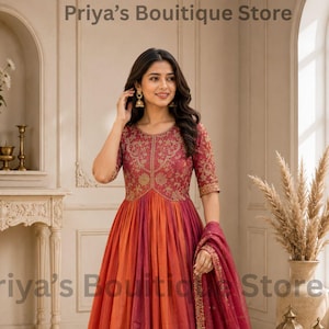 May include: A floor-length dress featuring a bodice with intricate gold embroidery and a skirt with vertical panels of orange and deep red. The dress includes a matching sheer red dupatta with gold border detailing and small gold accents.