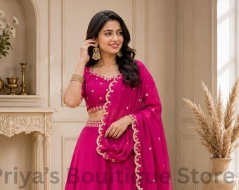 Könnte beinhalten: Ein leuchtend fuchsiafarbenes Lehenga-Choli-Set bestehend aus einer ärmellosen Bluse, einem bodenlangen Rock und einem passenden transparenten Dupatta. Das Kleidungsstück ist mit aufwendigen Goldstickereien am Ausschnitt und Saum verziert.