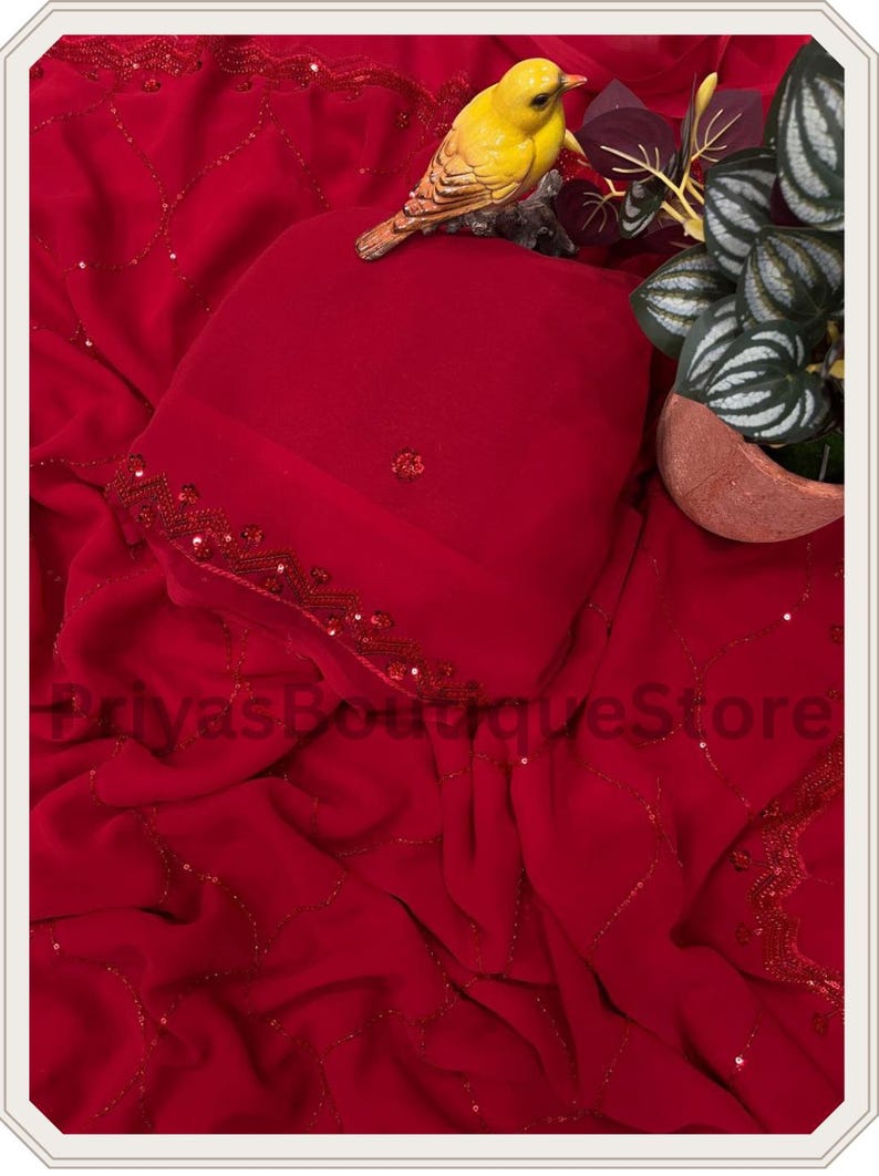 May include: A vibrant red fabric featuring a delicate pattern of thin, shimmering lines and small sequins. The material is draped with soft folds and includes a decorative border with intricate red beadwork. The text PriyasBoutiqueStore is visible.