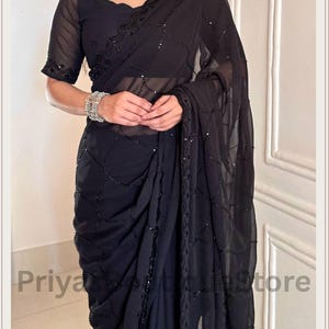 May include: A black saree featuring a sheer fabric with a delicate grid pattern of small black sequins. The garment includes a matching black blouse with short sleeves and a scalloped neckline, both adorned with intricate black sequin embroidery.