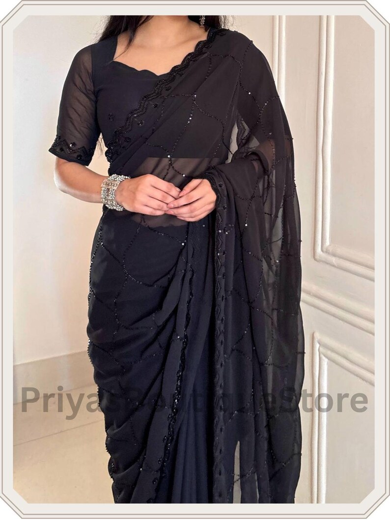 May include: A black saree featuring a sheer fabric with a delicate grid pattern of small black sequins. The garment includes a matching black blouse with short sleeves and a scalloped neckline, both adorned with intricate black sequin embroidery.