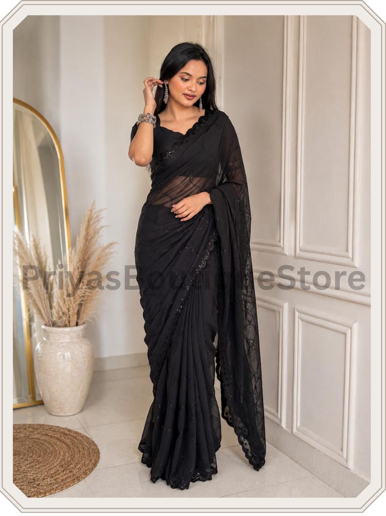 May include: A black saree featuring a sheer fabric with intricate tonal embroidery and sequin embellishments along the border and pallu. The garment is paired with a matching black short-sleeved blouse. The text PriyasBoutiqueStore is visible.