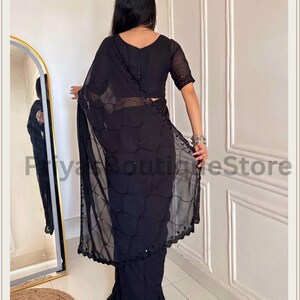 May include: A black saree featuring a sheer pallu with a delicate grid pattern and small reflective embellishments. The garment includes a matching black blouse with short sleeves and a scalloped border along the edge of the draped fabric.