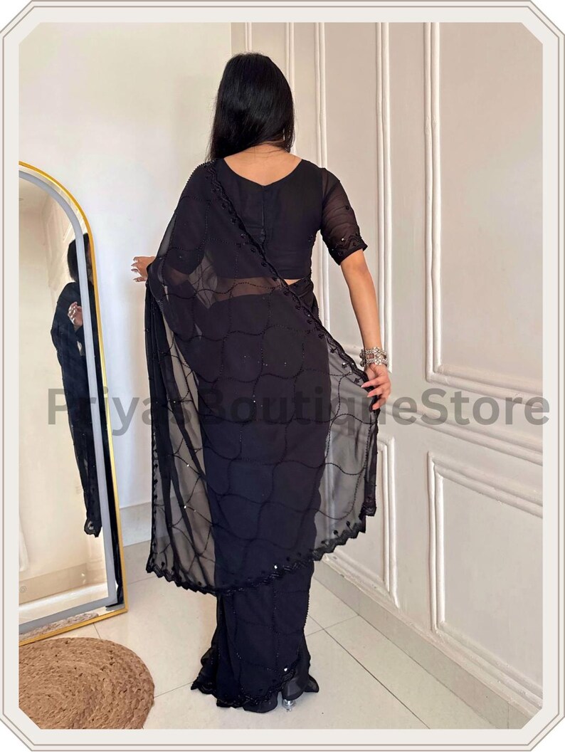 May include: A black saree featuring a sheer pallu with a delicate grid pattern and small reflective embellishments. The garment includes a matching black blouse with short sleeves and a scalloped border along the edge of the draped fabric.