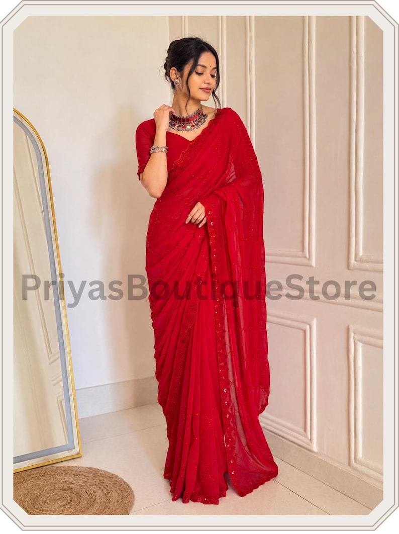 May include: A vibrant red saree featuring delicate embroidery along the border and subtle sequin embellishments throughout the fabric. The garment is paired with a matching short-sleeved blouse, creating a cohesive and elegant ensemble.