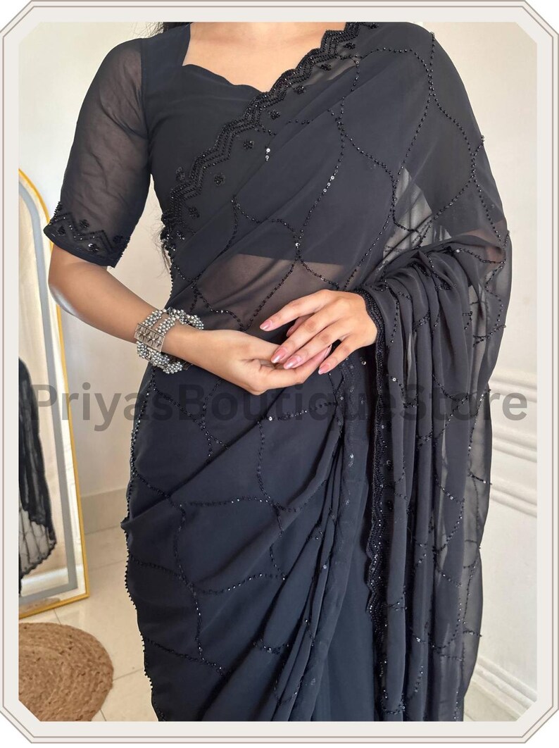 May include: A charcoal black saree featuring a sheer, lightweight fabric with an intricate, repeating lattice pattern created by small black beads and sequins. The garment includes a matching blouse with short sleeves and a scalloped, beaded neckline.