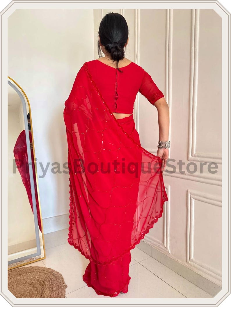 May include: A vibrant red saree featuring a sheer fabric with delicate sequin embroidery in a wavy pattern and a scalloped border. The ensemble includes a matching red blouse with short sleeves and a button-down back detail. Text reads PriyasBoutiqueStore.