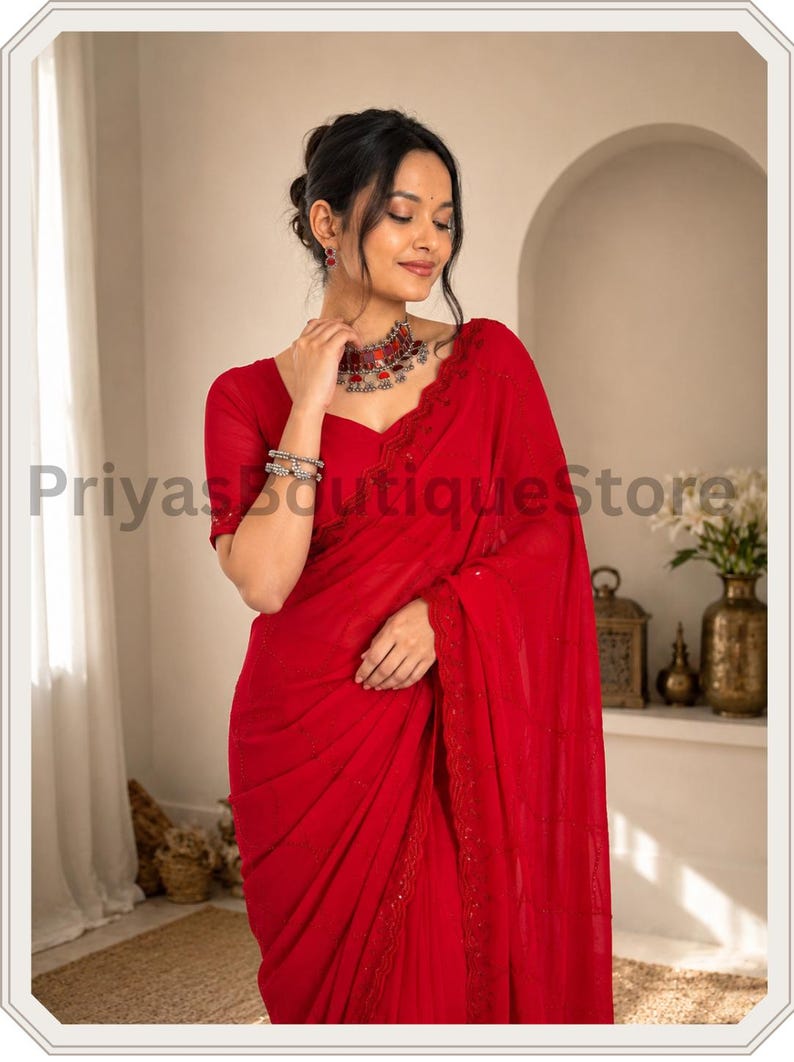 May include: A vibrant red saree featuring delicate embroidery along the border, paired with a matching short-sleeved blouse. The ensemble is accessorized with a silver-toned necklace and stacked bracelets, creating a cohesive and elegant appearance.