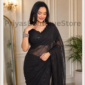 May include: A black saree featuring a sheer fabric with intricate black sequin embroidery in a geometric pattern. The garment includes a scalloped neckline on the blouse and a matching black border adorned with detailed sequin work throughout.