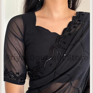 May include: A black saree featuring sheer fabric with intricate black beadwork and sequin embroidery along the borders and across the body. The blouse has short sheer sleeves and a square neckline, with the text PriyasBoutiqueStore visible.