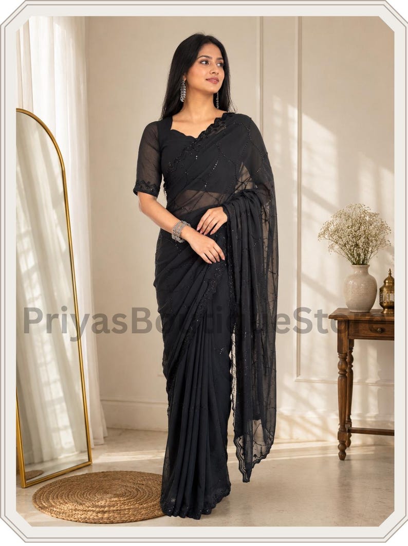 May include: A black saree featuring a sheer fabric with intricate tonal embroidery and subtle sequin embellishments. The garment includes a matching short-sleeved blouse with a scalloped neckline and a draped pallu that falls gracefully to the floor.