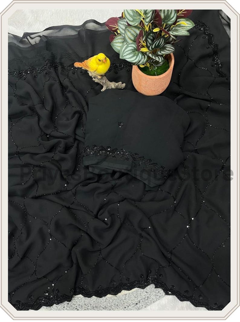 May include: A black chiffon saree featuring a delicate lattice pattern created with small black beads and sequins. The fabric is draped in soft folds, showcasing a decorative border with intricate beadwork and a matching black blouse piece.