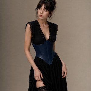 May include: A black dress featuring a deep V-neckline with lace trim, cap sleeves, and a full-length skirt. A structured, dark blue corset with a pointed hemline is worn over the dress. A black lace garter is visible on the upper thigh area.