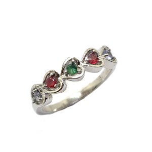 Peut inclure: Une bague argentée présentant une série de cinq sertissages en forme de cœur disposés en rangée. Chaque cœur contient une petite pierre précieuse ronde aux couleurs alternées, incluant violet clair, rouge, vert, rouge et violet clair.