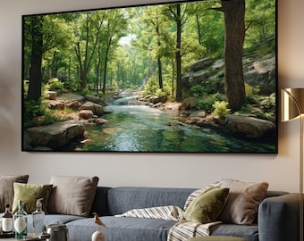 May include: A large rectangular wall art print featuring a lush forest landscape with a flowing stream, rocky banks, and tall green trees. The artwork is displayed in a thin black frame, mounted on a plain wall above a gray sofa with cushions.