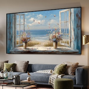 May include: A framed painting showing an open window with a beach view. The window frames are faded blue, with vases of flowers on the sill. Butterflies are seen in the sky above the sea. The artwork is displayed above a blue sofa.