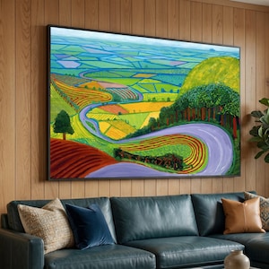 May include: A large rectangular landscape painting in a black frame featuring a winding purple road through a vibrant countryside. The scene displays rolling hills, green and yellow agricultural fields, and a dense forest under a blue sky.