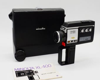 Może przedstawiać: Czarna kamera filmowa Minolta XL-400 ze srebrnym panelem bocznym, czarnym futerałem z logo Minolta, oddzielną czarną osłoną obiektywu oraz białą instrukcją obsługi zatytułowaną MINOLTA XL-400 MODE D'EMPLOI z rysunkiem liniowym kamery.