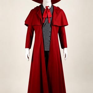 May include: A red costume ensemble on a mannequin. The outfit includes a long coat, a wide-brimmed hat, and a matching necktie. The coat has a cape-like design. The mannequin is wearing a gray vest and white gloves. The costume is a theatrical or historical style.