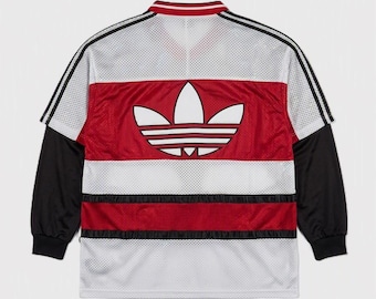 May include: A white, red, and black long-sleeve mesh jersey featuring a large white Adidas trefoil logo on the back. The garment has a ribbed collar, black sleeves with three stripes, and horizontal red and black bands across the torso area.