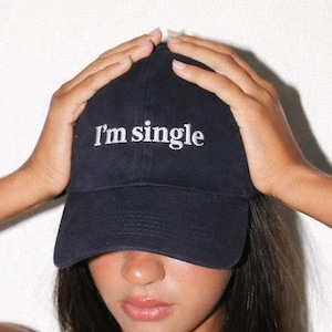 Könnte beinhalten: Eine dunkelblaue Baseballkappe mit dem in Weiß gestickten Text "I'm single", der mittig auf der Vorderseite platziert ist. Die Kappe hat einen gebogenen Schirm und eine strukturierte Krone aus einem festen Stoff mit sichtbaren Nähten.