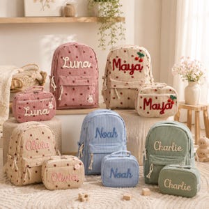 Könnte beinhalten: Eine Auswahl an Rucksäcken und Lunch-Taschen aus Cord in verschiedenen Farben, darunter Rosa, Beige und Blau. Jede Tasche ist mit einem Namen in einer Kontrastfarbe bestickt. Einige Taschen haben ein Tupfenmuster oder dekorative Akzente wie Kirschen.