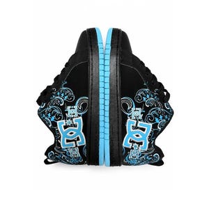 May include: A pair of black sneakers featuring a light blue DC logo on the side, accented with intricate white and light blue swirling patterns. The shoes have black laces, a black upper, and a light blue rubber sole with a textured tread pattern.