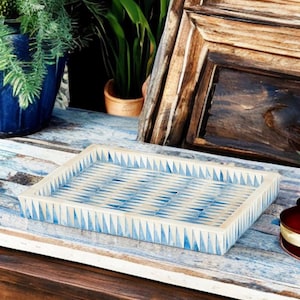 May include: A rectangular tray featuring a repeating geometric pattern of blue triangles set against a cream-colored background. The tray has raised edges and a smooth, flat base, showcasing a consistent arrangement of small, pointed shapes.
