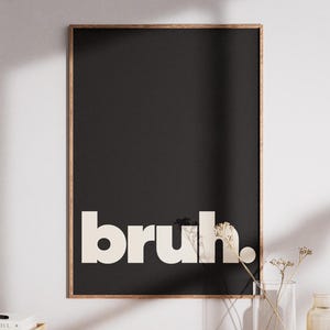 May include: A rectangular wall art print in a wooden frame featuring a solid black background with the word bruh. printed in large, bold, off-white sans-serif lowercase letters centred at the bottom of the vertical composition.