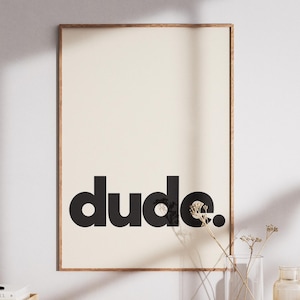 Könnte beinhalten: Ein rechteckiges Wandbild in einem dünnen Holzrahmen mit cremefarbenem Hintergrund, auf dem das Wort dude. in fetter, schwarzer, serifenloser Typografie in Kleinbuchstaben mittig in der Komposition abgedruckt ist.