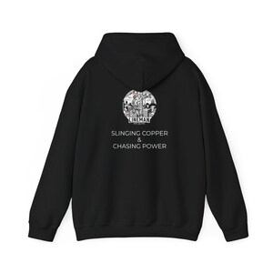Puede incluir: Sudadera con capucha negra con capucha y mangas largas. La parte trasera presenta un gráfico circular con la palabra "LINEMAN" y el texto "SLINGING COPPER & CHASING POWER" en blanco.