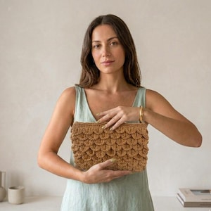 Peut inclure: Une pochette en crochet de couleur beige avec un motif texturé en écailles superposées. Cet accessoire rectangulaire est fabriqué en fibres tressées et présente un design festonné répétitif sur toute la surface avant du sac.