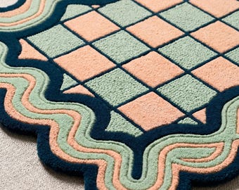 May include: A tufted rug featuring a central rectangular grid of alternating light green and peach squares. The rug is framed by a thick, dark navy blue border with wavy, undulating edges in alternating bands of light green and peach yarn.