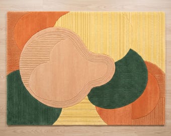 May include: A rectangular area rug featuring an abstract composition of overlapping organic shapes in shades of orange, yellow, peach, and dark green. The design incorporates varied textures, including smooth surfaces and sections with raised linear ridges.
