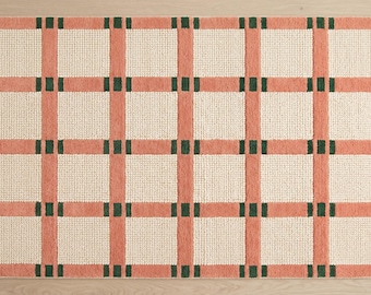 May include: A rectangular area rug featuring a grid pattern of peach-colored vertical and horizontal bands. The intersections of these bands are accented with small, dark green rectangular blocks, while the squares between are off-white.