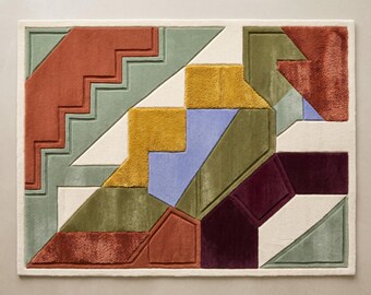 May include: A rectangular area rug featuring a geometric pattern composed of tufted sections in shades of terracotta, sage green, mustard yellow, periwinkle blue, deep plum, and cream. The design includes varied shapes with raised borders.