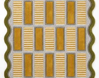 May include: A rectangular area rug featuring a scalloped olive green border. The interior displays a grid of alternating solid mustard yellow rectangles and white and mustard yellow striped rectangles, all set against a light gray background.