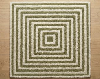 May include: A square rug featuring a concentric pattern of alternating olive green and cream-colored stripes. The design consists of multiple nested square frames that radiate outward from a solid olive green square center, creating a geometric effect.