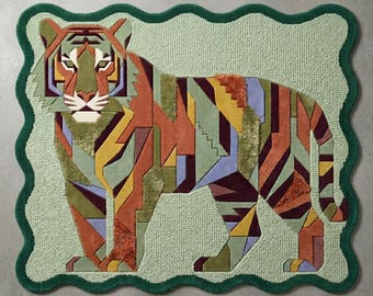 May include: A rectangular rug with a scalloped dark green border featuring a stylized tiger illustration. The tiger is composed of geometric patches in shades of orange, olive green, yellow, purple, and brown against a light green background.