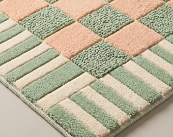 May include: A tufted rug featuring a checkered pattern of sage green and soft peach squares. The border consists of alternating rectangular stripes in sage green and cream, creating a structured geometric design with a textured pile surface.