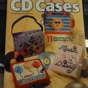 May include: A book cover titled "CD Cases" by Needlecraft, featuring designs by Ronda Bryce. The cover showcases several colorful, handcrafted CD cases, including a purple guitar case, a pink music diary, and a red balloon case. The cases are designed to hold favorite CDs.