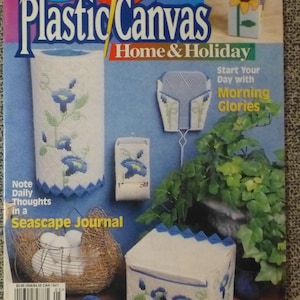 May include: A magazine cover titled "Plastic Canvas Home & Holiday" featuring various plastic canvas projects. The projects include a tissue holder, a box, and a bird's nest. The magazine's text includes "Quick-to-Stitch Holiday Projects" and "Start Your Day with Morning Glories."