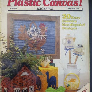 May include: Plastic Canvas! Magazine, issue number 1, March/April 1989. The cover features 30 easy country needlepoint designs, including a framed picture of a rooster with flowers, a jug with flowers, a house, a block with the letter H, an apple, and a basket with fruit.