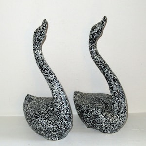 May include: Two black and white ceramic swan sculptures. The swans have a speckled finish and are posed with their necks curved.