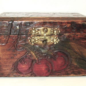 May include: A rectangular wooden box with a dark brown finish and a brass clasp. The box features carved cherry designs on the front and sides. The cherries are painted red, and the leaves are green.