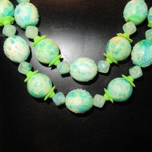 May include: A double strand necklace with green and blue beads. The beads are round and have a speckled pattern.