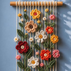 May include: A decorative wall hanging with a floral design. It features crocheted flowers in red, orange, yellow, pink, and white, with green leaves. The flowers are arranged on a cream-coloured background, suspended from a wooden dowel at the top and bottom, creating a textured display.